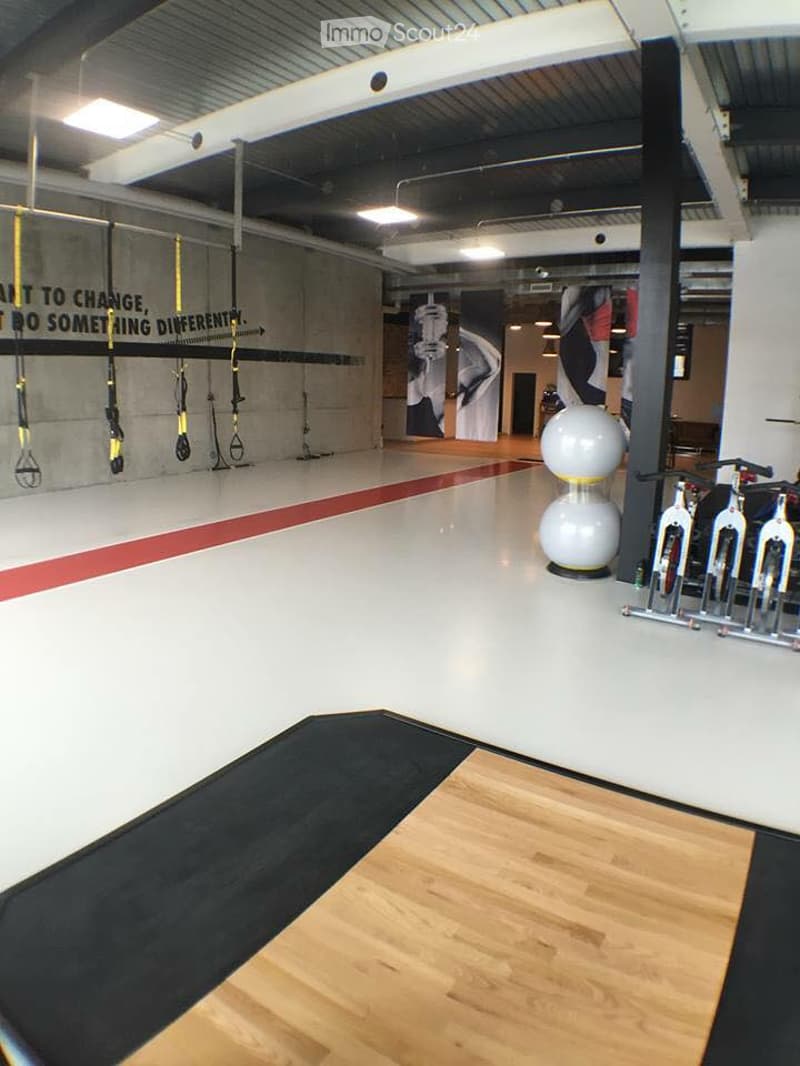 Modern fitness studio with wooden flooring, white walls, and various exercise equipment including a fitness ball, exercise bikes, and resistance bands.