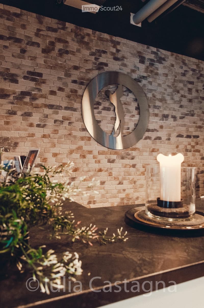 Bathroom with a decorative brick wall, a round mirror with a metallic frame, and a lit candle on a surface.