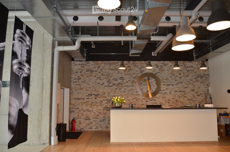 Modern reception area with exposed brick wall, reception desk, hanging pendant lights, and a decorative vase with flowers on the desk.