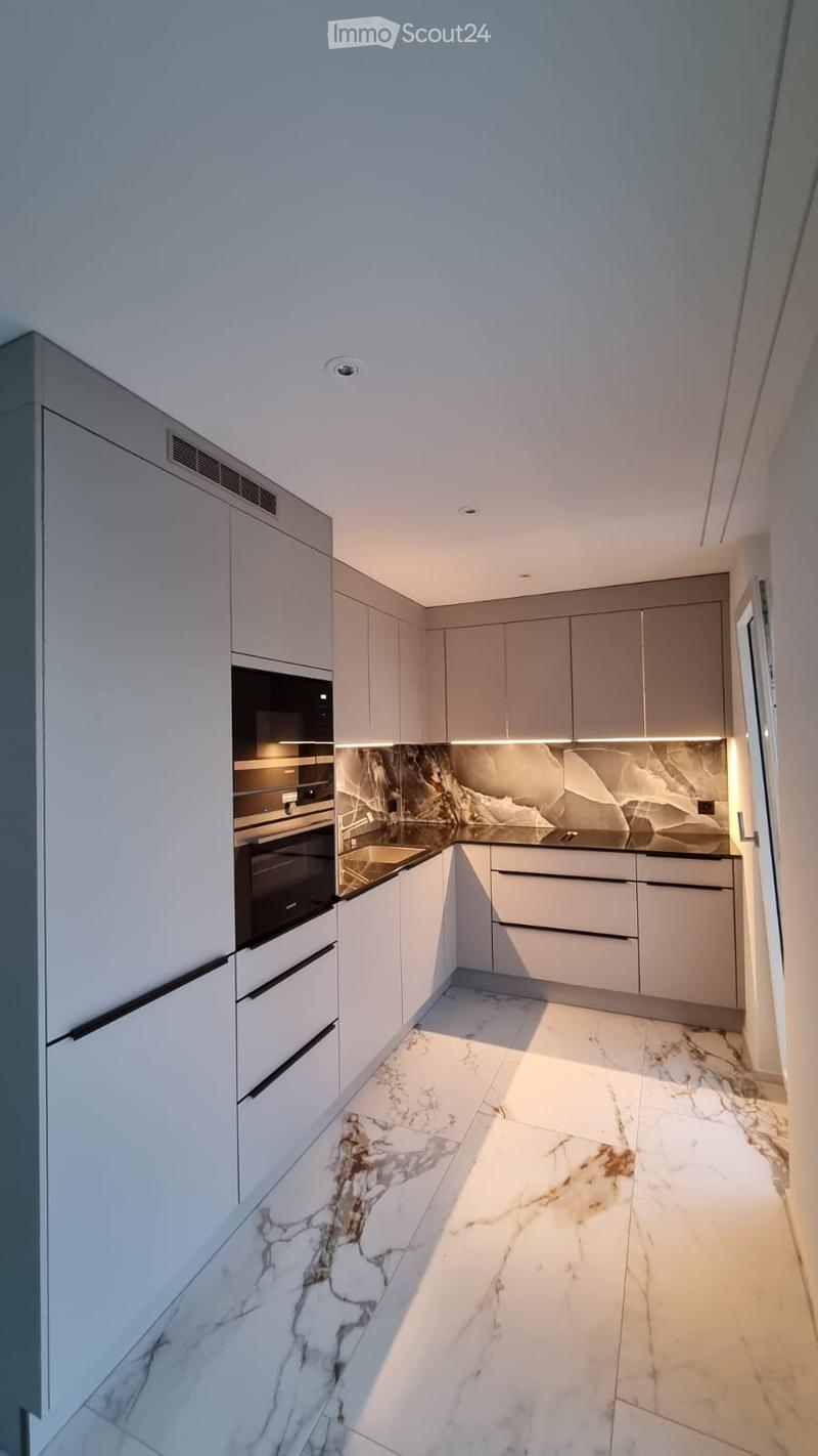 Modern kitchen with white cabinets, marble countertops, and a marble floor. Features an integrated oven and sleek design.