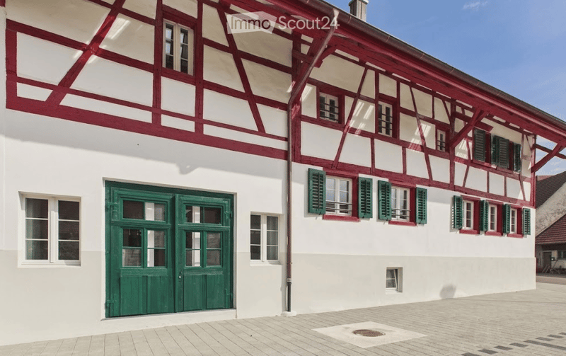 Traditional half-timbered building with white walls, red wooden beams, green shutters, and a green double door.