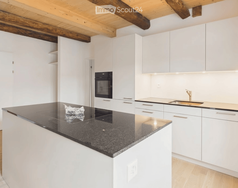Modern kitchen with white cabinets, a black granite island, and stainless steel appliances including an oven and sink.