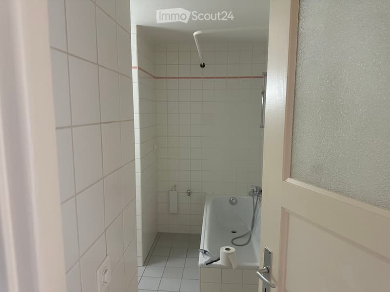 Bathroom with a bathtub, tiled walls, and a toilet paper roll on the edge of the tub.