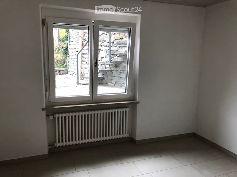 Empty room with white walls, tiled floor, window with view to stairs, white radiator