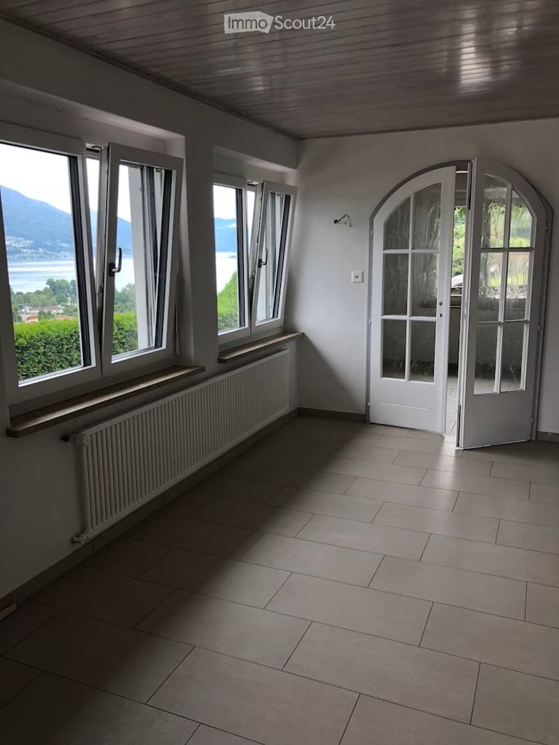 spacious room with windows, white floor, white walls, radiator, open door, view of the sea and mountains