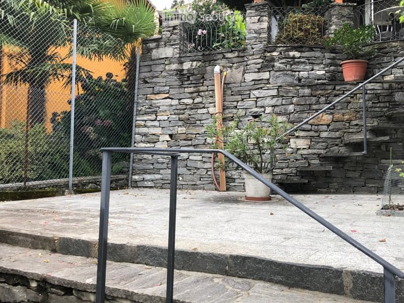 stone wall, metal railing, stairs, plants in pots, chain-link fence