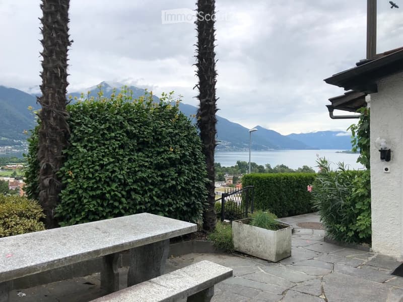 Outdoor seating area with a bench, a table, and a potted plant. View of mountains and a body of water in the background.