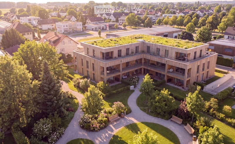 Aerial view of a modern, multi-story residential building with wooden facades and balconies, surrounded by greenery and pathways.