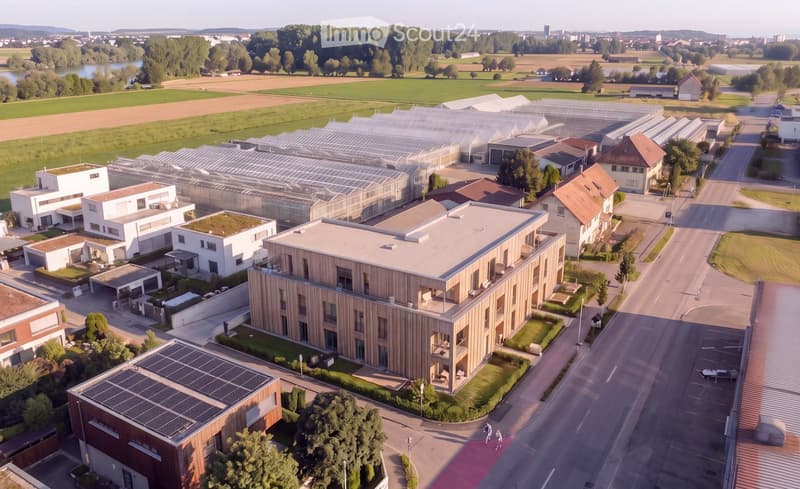 Aerial view of a modern residential complex with multiple buildings, green spaces, and greenhouses.