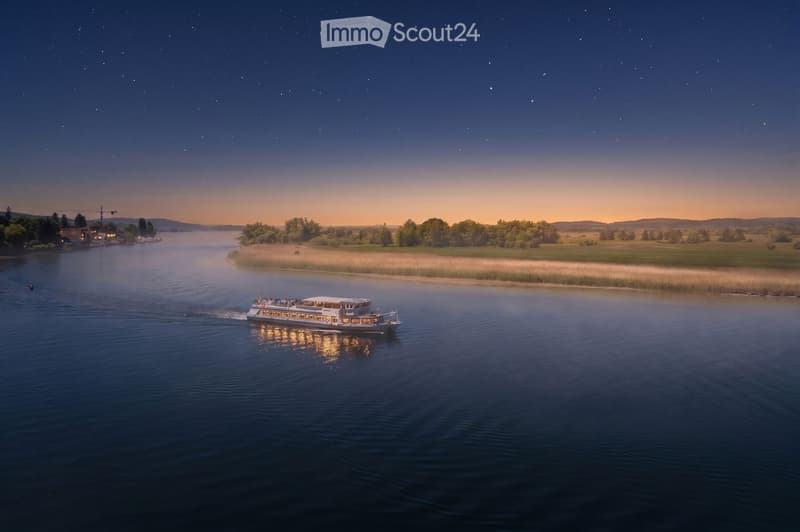 A serene river scene at sunset with a boat gliding on calm waters, surrounded by lush greenery and distant hills under a starry sky.