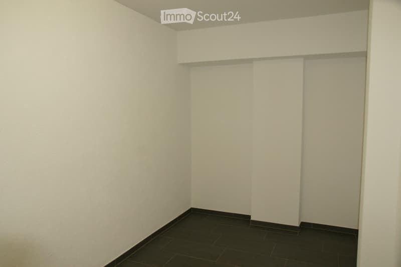 Completely empty room with bare white walls and dark tiled floor. No furniture or equipment.