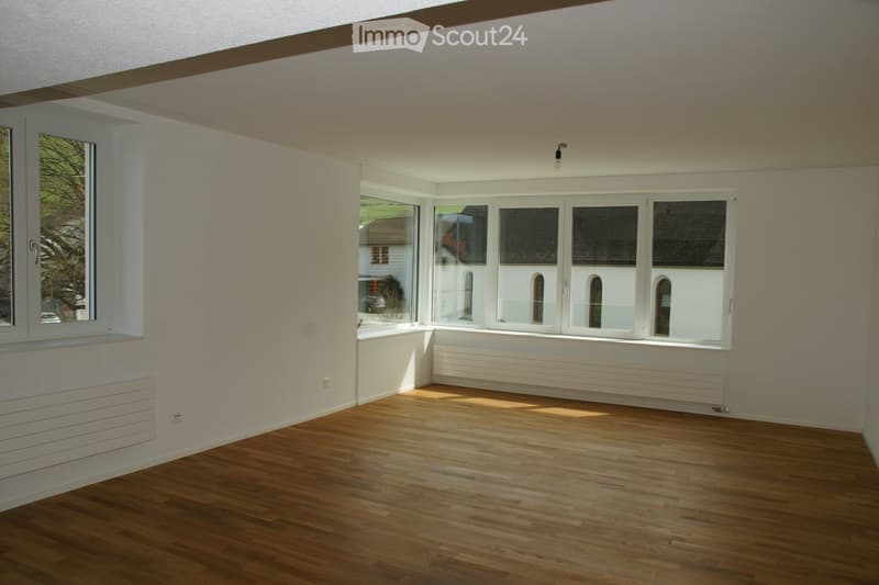 Empty room with wooden flooring, large windows, and radiators along the walls. No furniture or personal items are present.