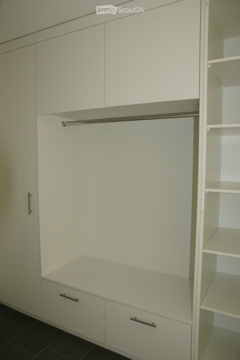 Empty closet with white cabinets, shelves, and drawers, featuring metallic handles.