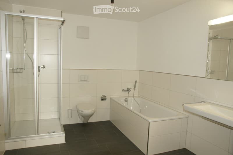 Modern bathroom with white tiles, a bathtub, toilet, sink, and a glass-enclosed shower. Features a large mirror above the sink and a dark tiled floor.
