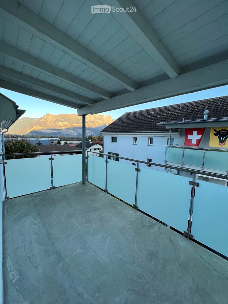 Balcony with a modern glass railing, concrete floor, and a view of mountains in the background.