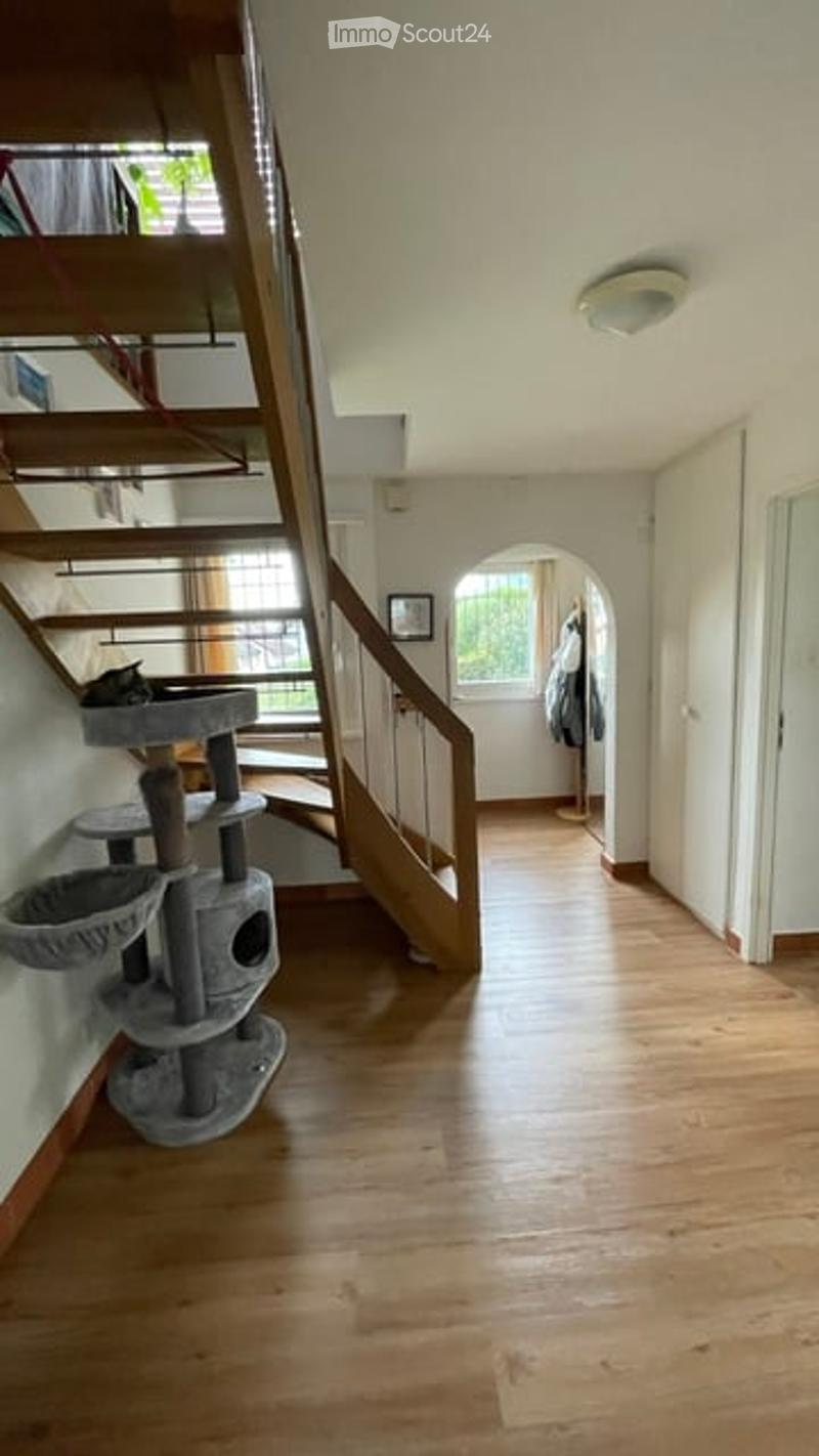 Spacious hallway with wooden flooring, staircase leading to an upper level, and a cat tree with a cat on it.