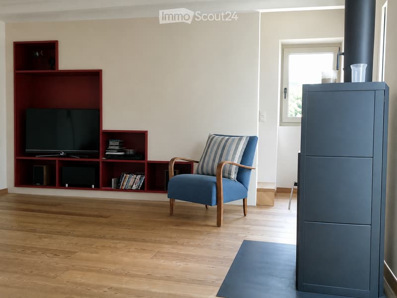 Modern living room with wooden flooring, a blue armchair, a red shelving unit with a TV, and a small table with a cup.