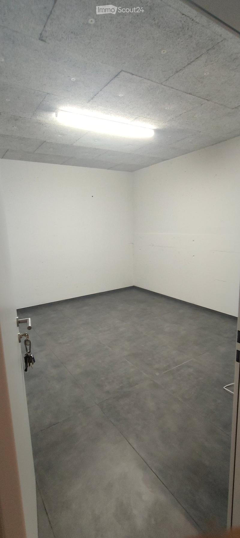 Empty room with grey tiled floor and white walls, featuring a single light fixture on the ceiling and a door with a key visible.