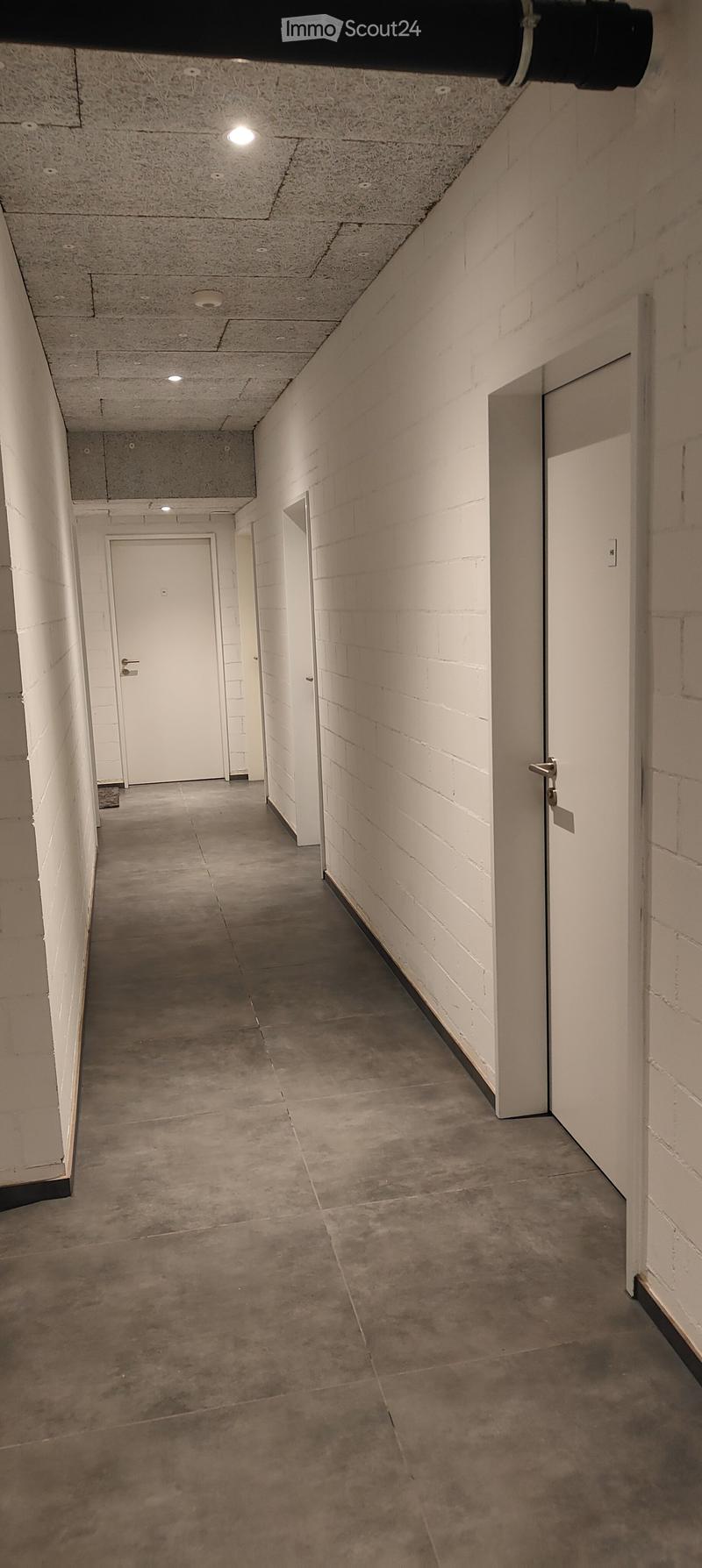 Empty hallway with concrete floors, white brick walls, and white doors at both ends.