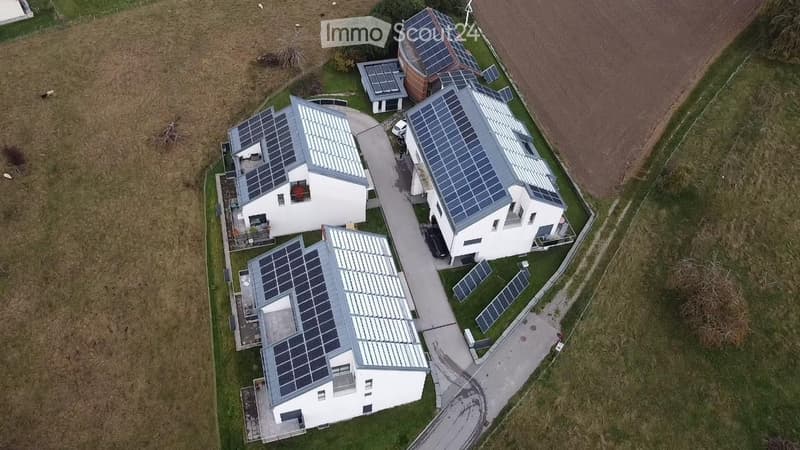 Aerial view of three modern houses with solar panels on the roofs, surrounded by a grassy area and a paved driveway.