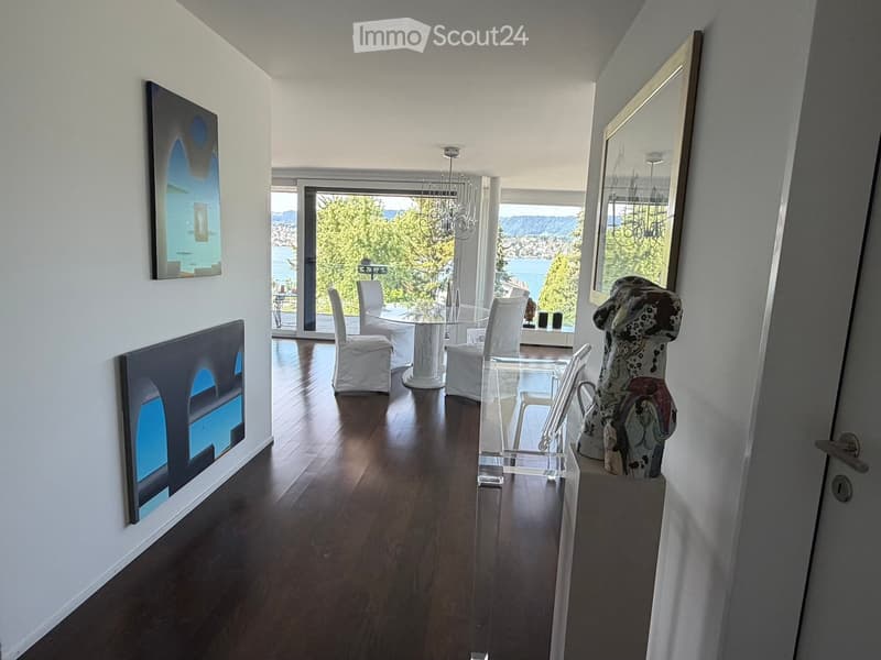 Modern dining area with hardwood floors, large windows offering a scenic view, a glass dining table with white chairs, a large mirror, and a decorative sculpture.