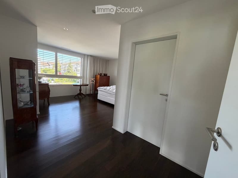 Bright bedroom with wooden flooring, large window with blinds, bed, small table, cabinet, and mirror cabinet.