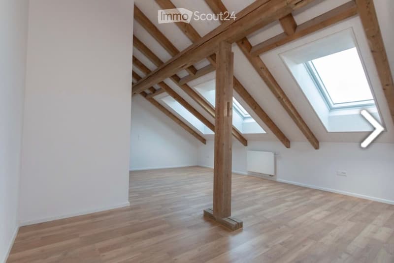 Empty attic room with wooden beams, skylights, and wooden flooring.