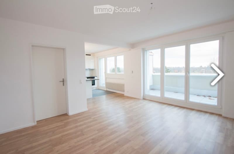 Bright, unfurnished living space with wooden flooring, large windows, and a sliding glass door leading to a balcony.