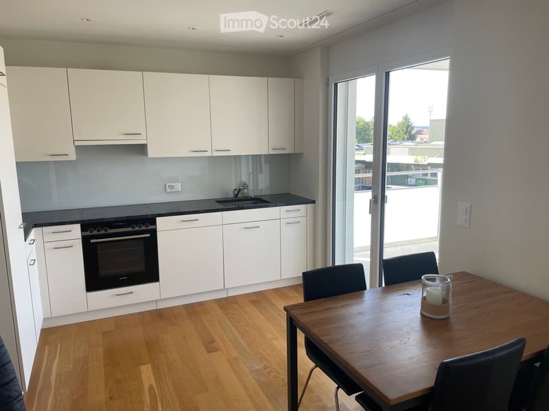 Modern kitchen with white cabinets, black countertops, and a wooden dining table with chairs. Features an oven, sink, and candle on the table.