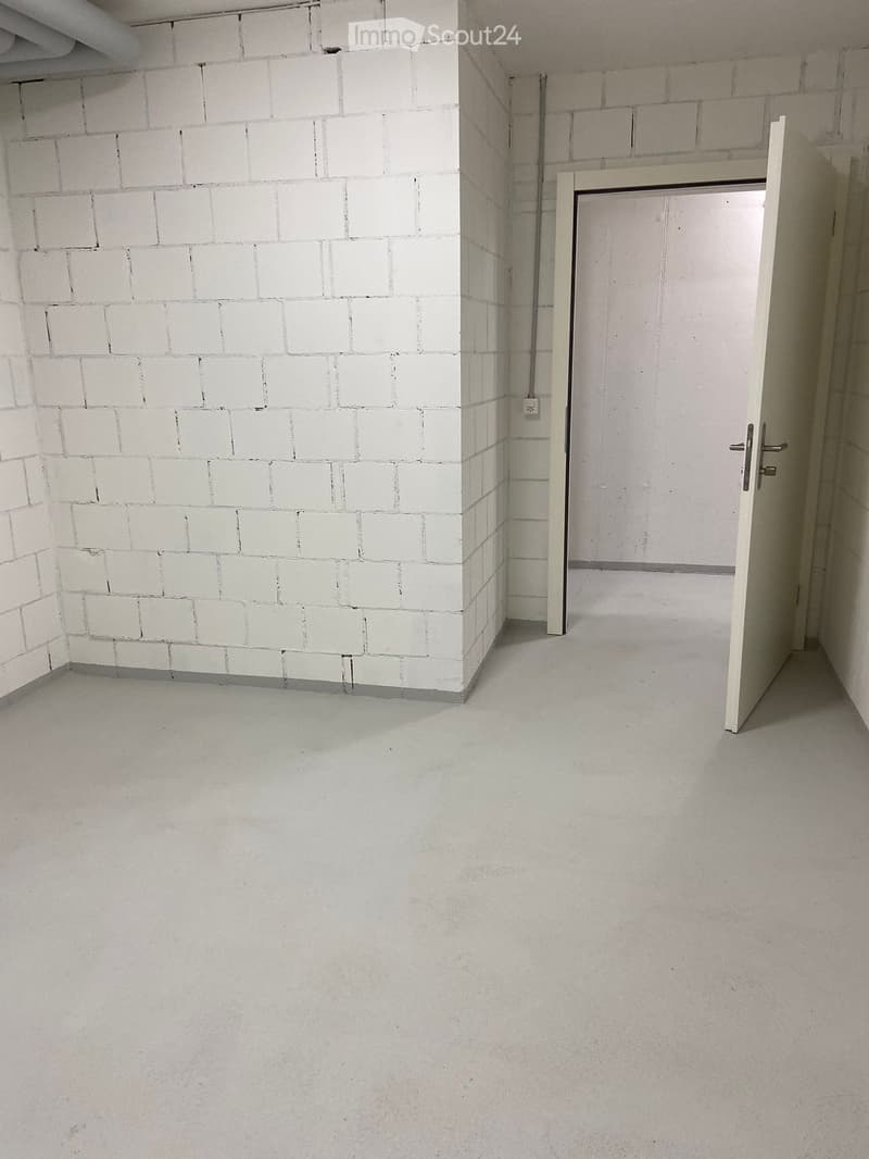 Empty room with white brick walls, grey concrete floor, and a single open door leading to another space.