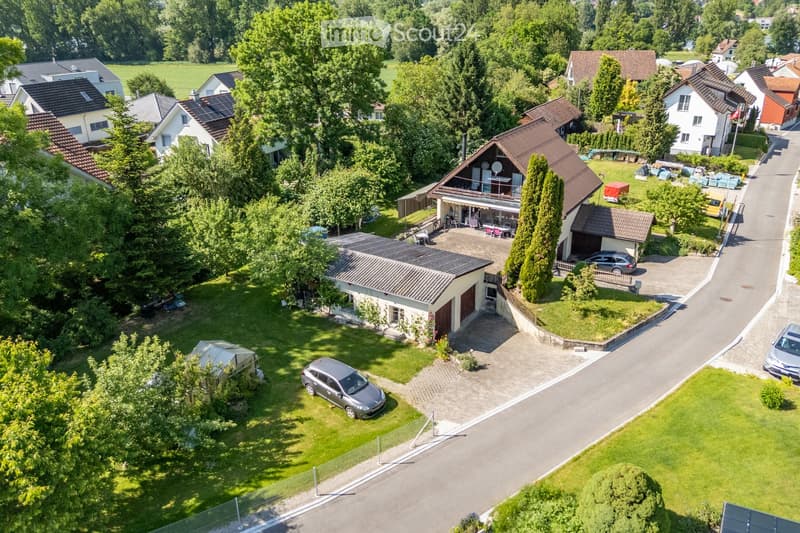 Aerial view of a residential neighborhood with multiple houses, gardens, driveways, and parked cars.