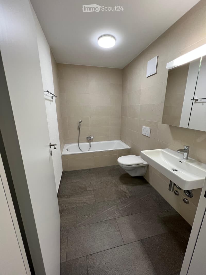 Modern bathroom with beige tiled walls, a bathtub, toilet, sink, and a mirrored cabinet.
