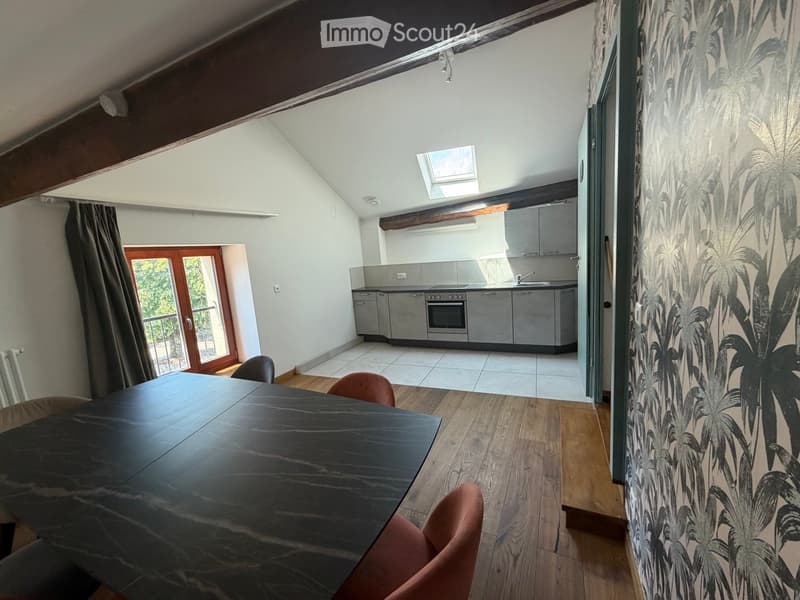 A modern, open-plan living and dining area with a sleek black dining table and chairs, leading to a contemporary kitchen with stainless steel appliances and cabinets.
