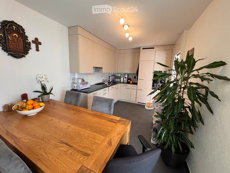 A modern kitchen and dining area with a wooden dining table, grey chairs, light-colored cabinets, and various appliances.