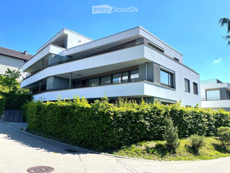 Modern two-story house with white facade, large windows, balconies, and surrounding greenery.