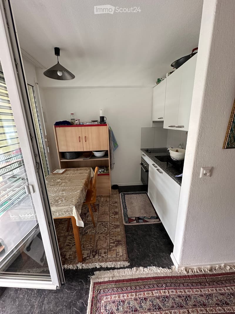 A compact, well-lit kitchen and dining area with white cabinets, a small dining table with a chair, and various kitchen appliances.