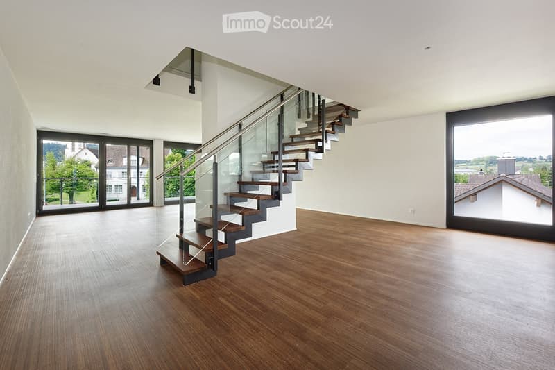 Modern hallway with wooden flooring, glass staircase, large windows, and open space.