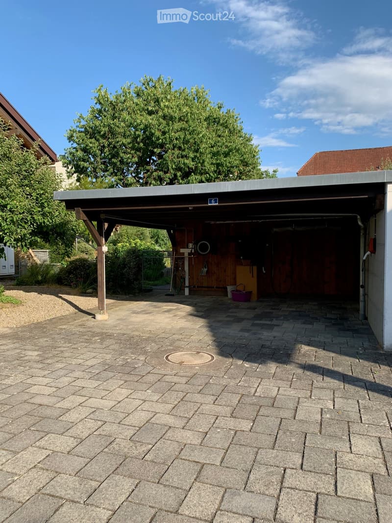 Paved outdoor area with a covered garage entrance, a tree, and surrounding greenery.