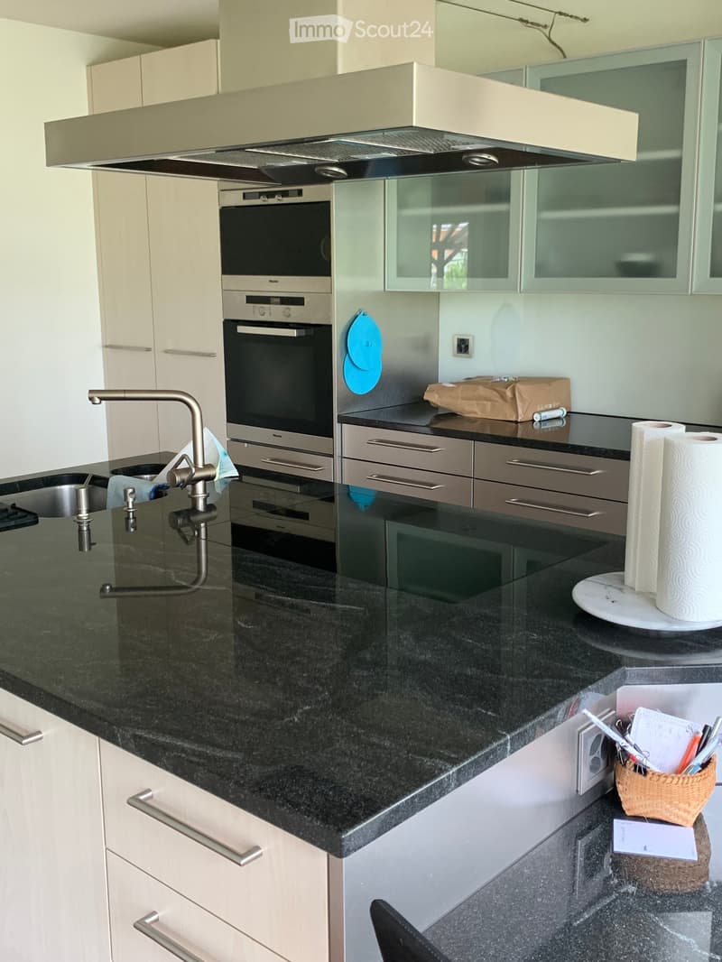 Modern kitchen with black granite countertops, white cabinets, stainless steel oven, and a sleek faucet. Includes a paper towel holder, wicker basket, and various small items on the counter.