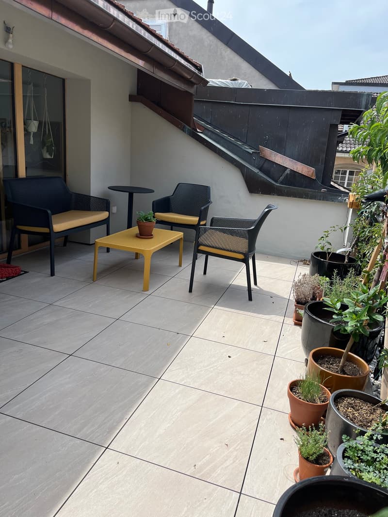 Balcony with tiled floor, yellow table, black chairs, and several potted plants.