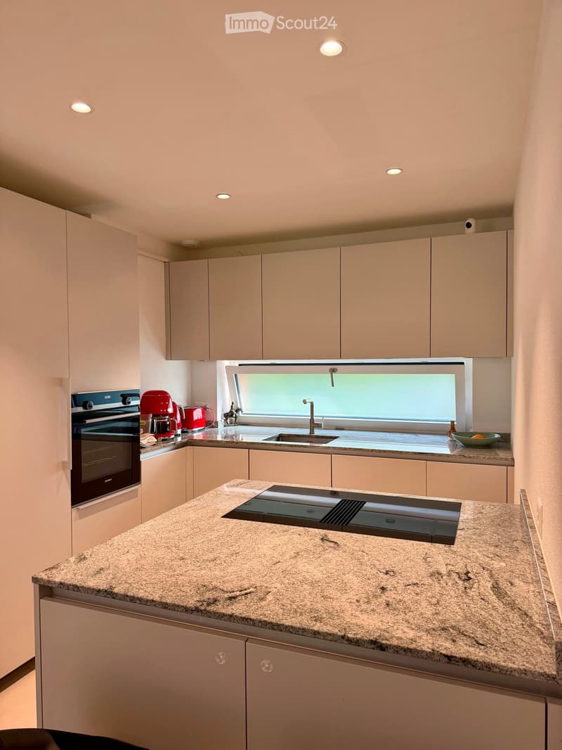 Modern kitchen with light-colored cabinets, granite countertop, built-in oven, coffee maker, and a sink with a window above it.