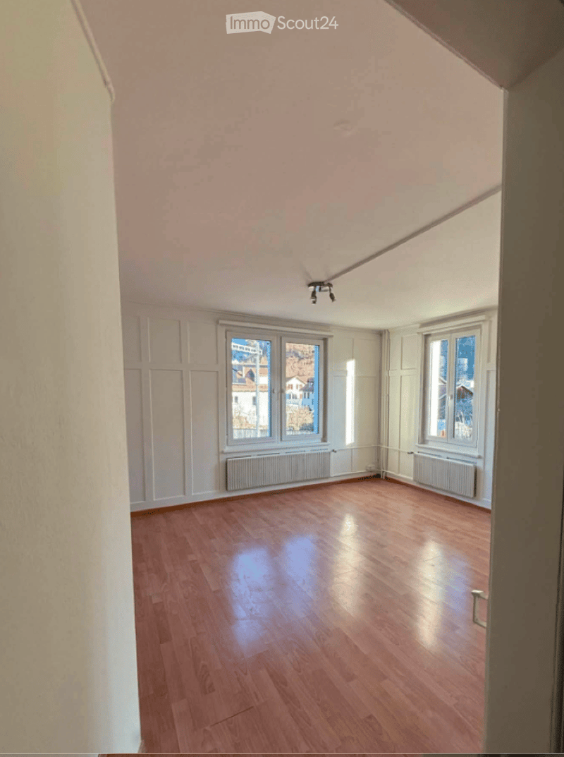 Empty room with wooden flooring, white walls, and large windows offering a view of the outside. No furniture or equipment is present.