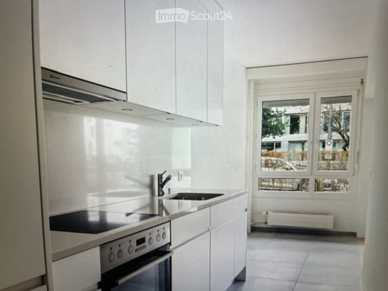 Modern, minimalist kitchen with white cabinets, stainless steel appliances, and a large window providing natural light.