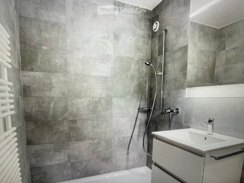 Modern bathroom with grey tiled walls, a white sink, a large mirror, and a shower with a handheld sprayer.