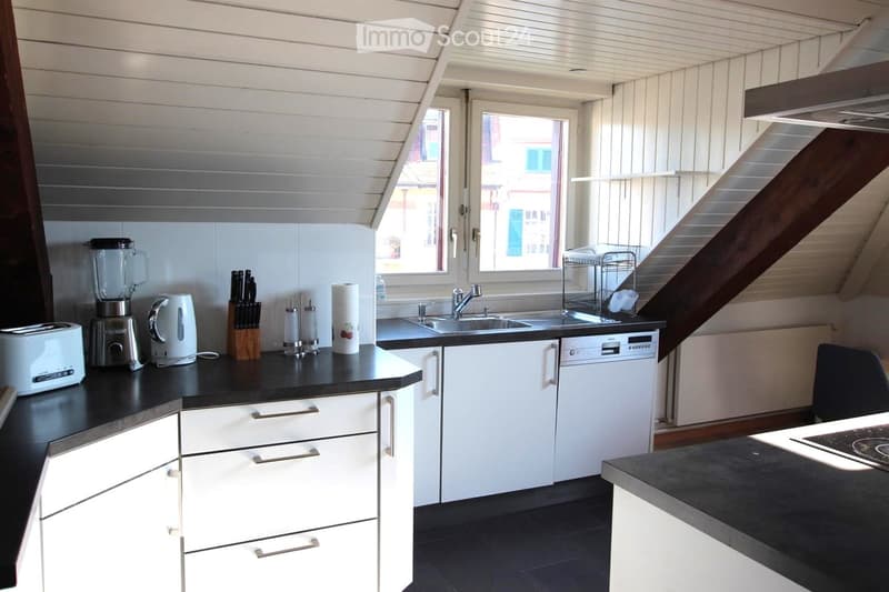 Modern kitchen with white cabinets, black countertops, and stainless steel appliances. Features include a toaster, blender, electric kettle, knife block, dishwasher, sink, and paper towel holder.