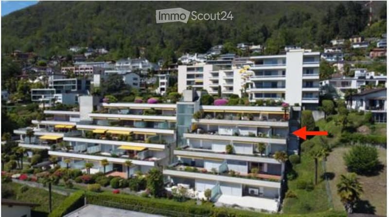 Aerial view of a multi-story residential complex with numerous balconies and terraces, surrounded by greenery and neighboring buildings.