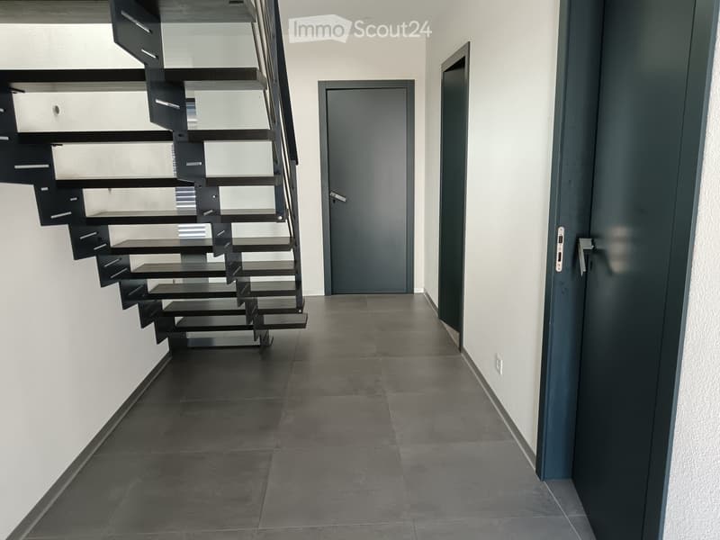 Modern hallway with dark tiled floor, white walls, and a sleek black staircase leading upwards. Two doors are visible, one on each side of the hallway.