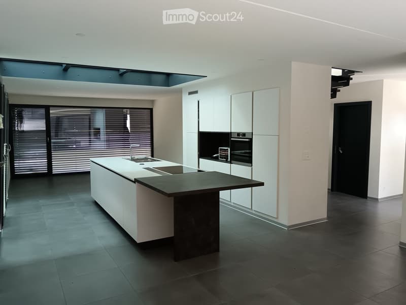 Modern kitchen with white cabinets, a central island, and built-in appliances including a sink, oven, and microwave. The space features large windows with blinds and a sleek, contemporary design.