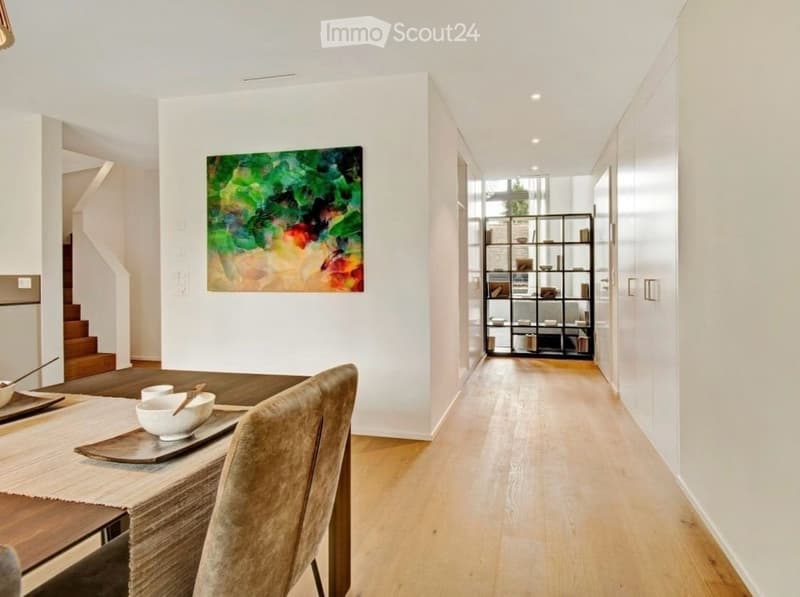 Modern dining area with a wooden table, chairs, and a colorful abstract painting on the wall. A sleek black shelving unit is visible in the background.