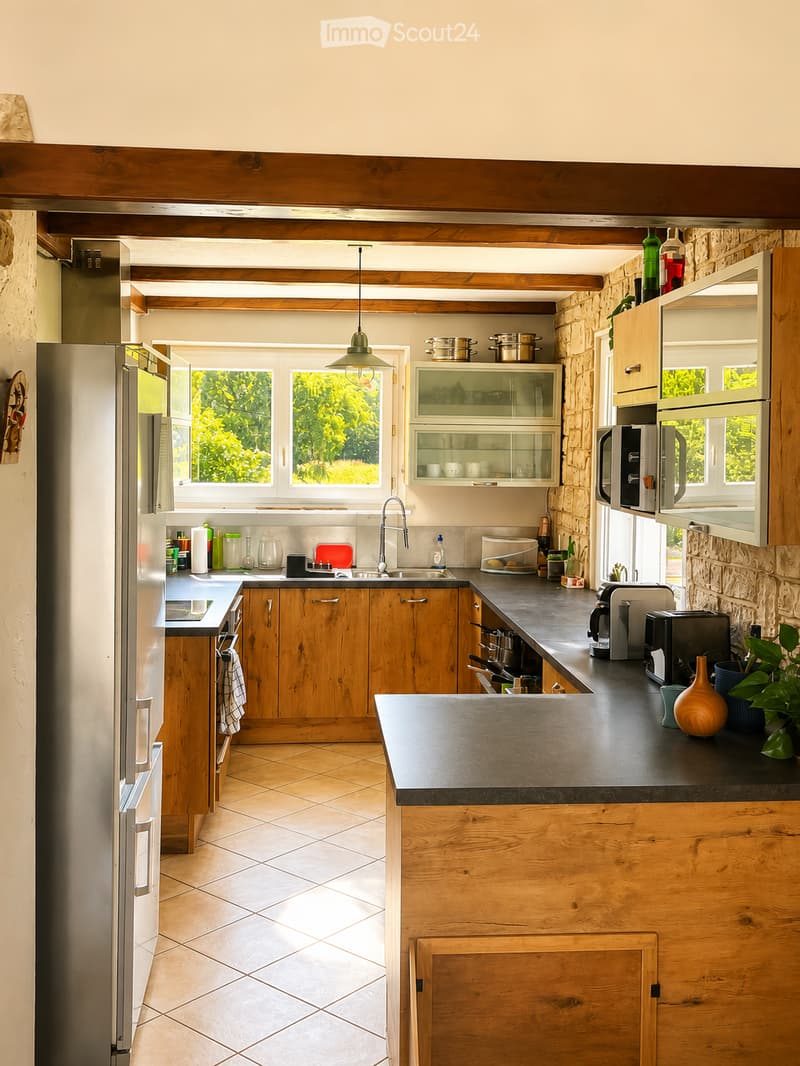 Bright kitchen with wooden cabinets, stainless steel appliances, and a central island. Features a sink, microwave, and various kitchen items on the counters.